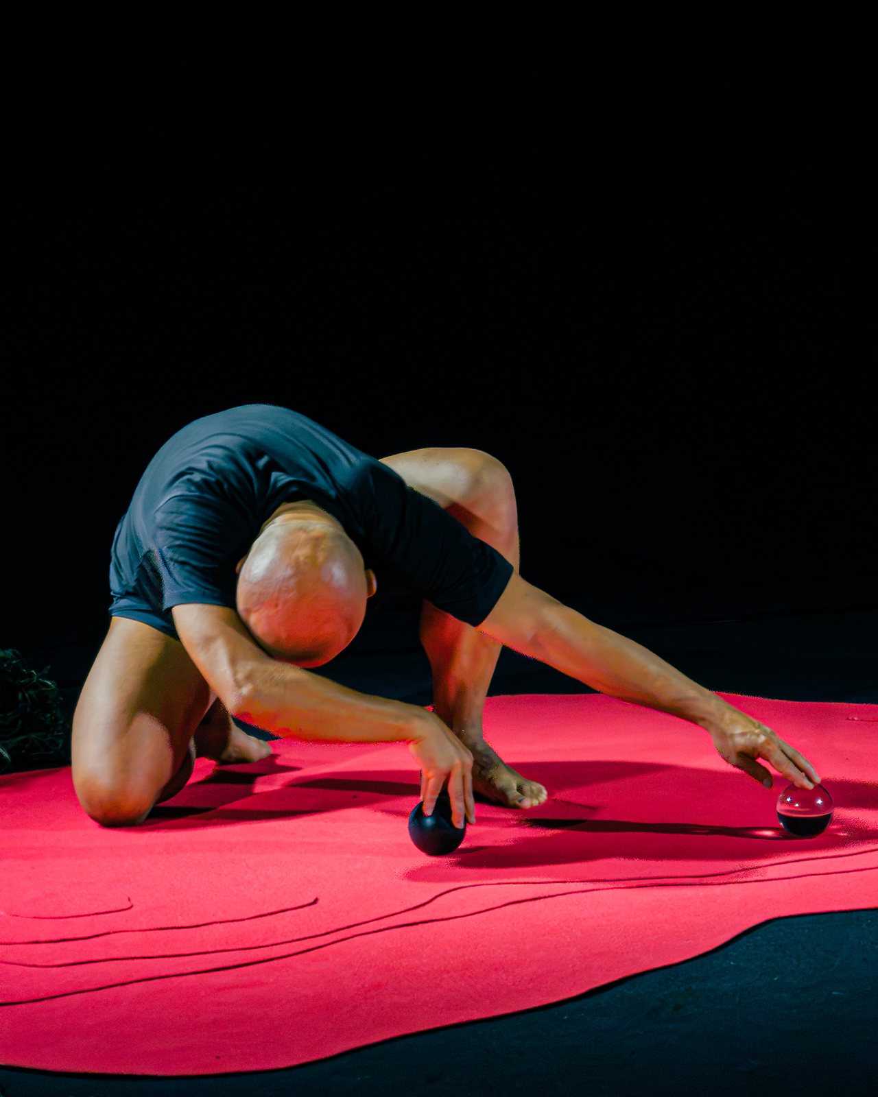 Performer curled over the red floor, hands reaching towards two spheres