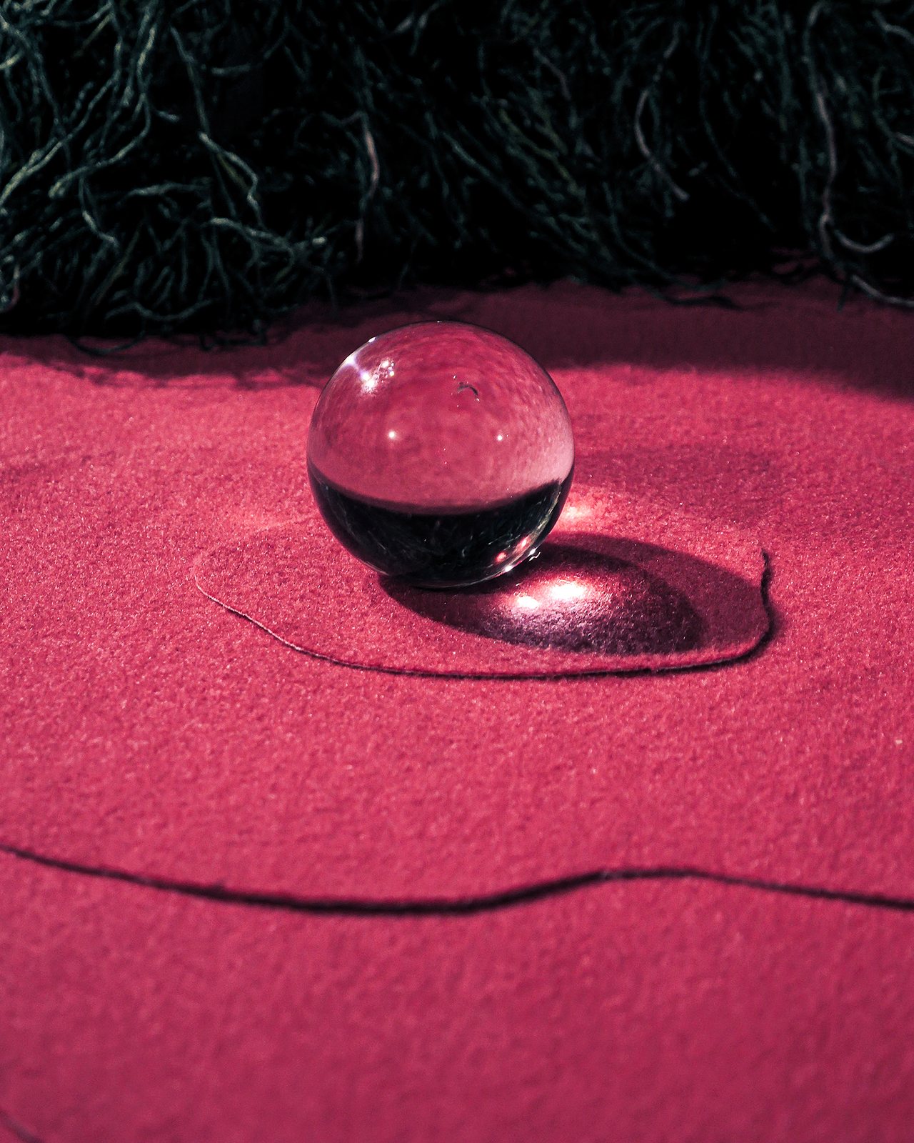 Transparent sphere resting on the red felt floor, casting a long shadow