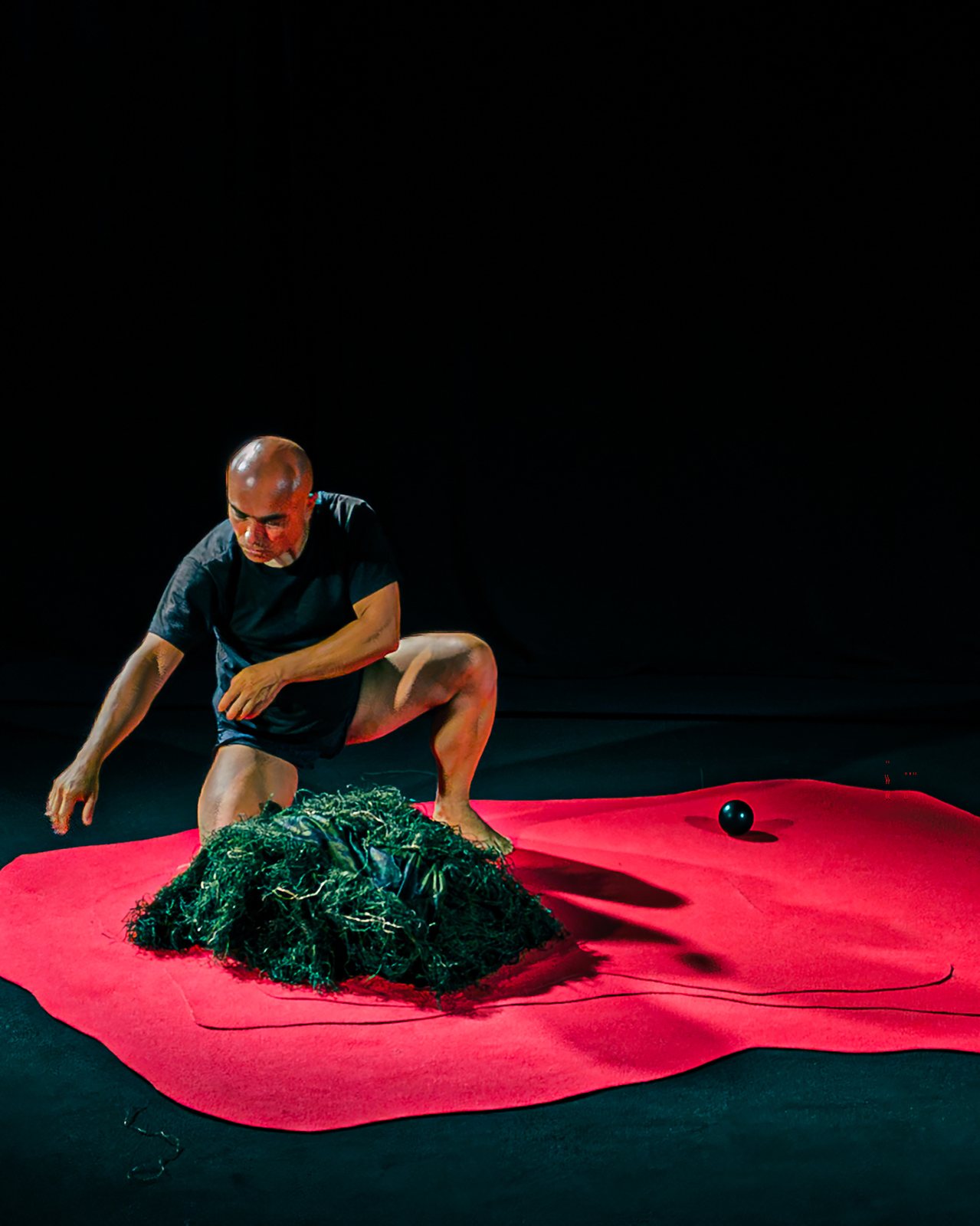 Performer stepping over the mass of green fibres on the red floor