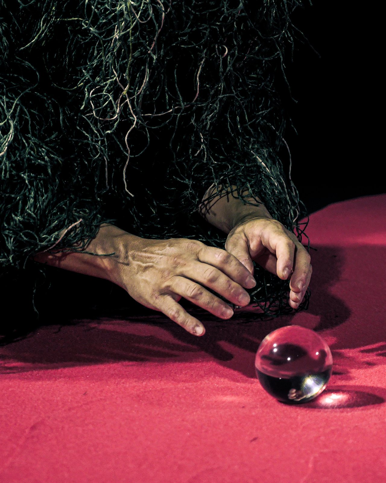 Hand emerging from the green mass reaching towards a glass sphere