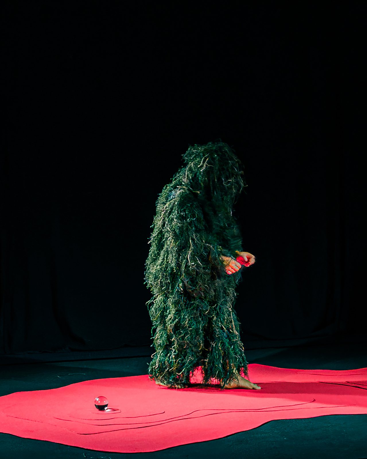 Figure covered in green fibres standing upright on the red floor