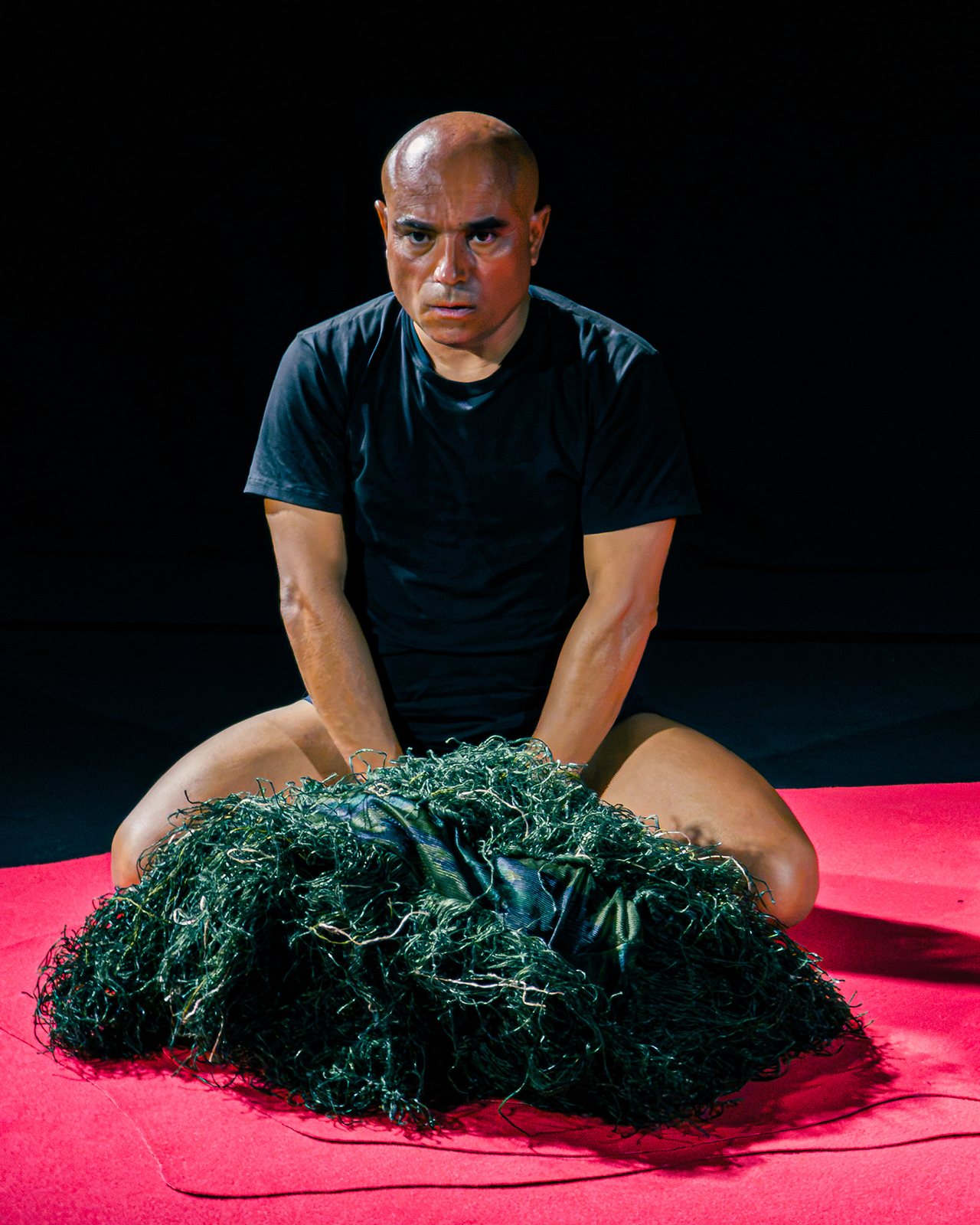 Performer seated frontally with the green mass resting on his lap